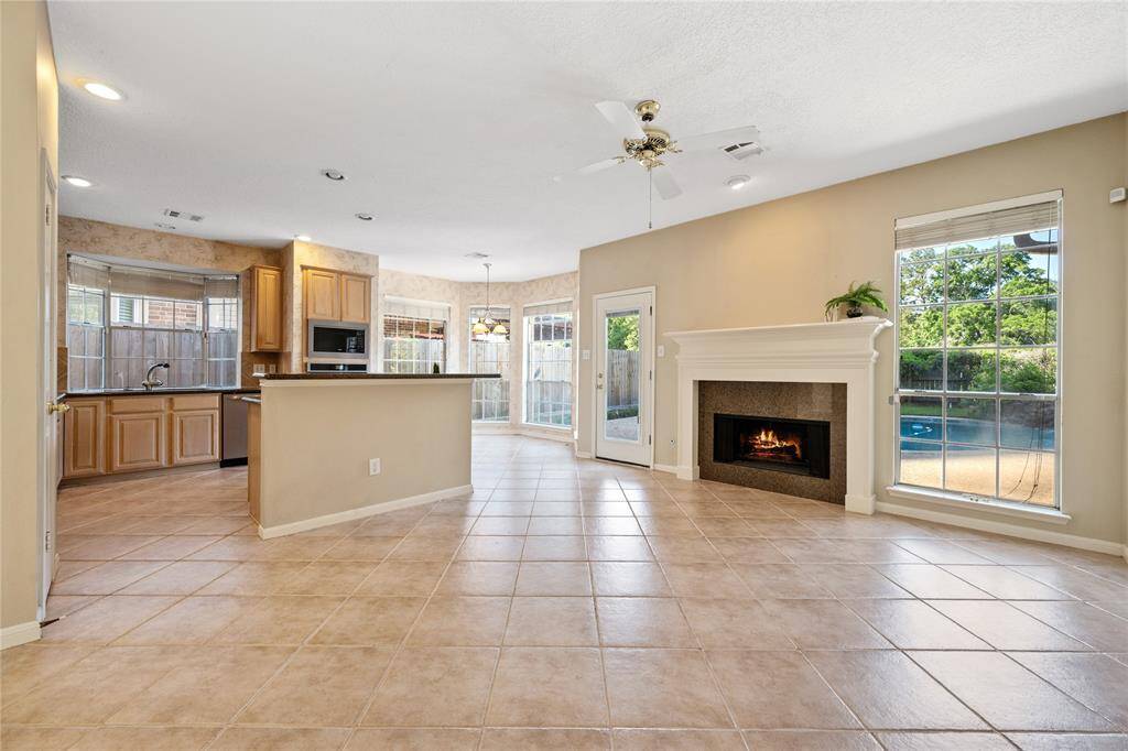 Bright and spacious open-concept living area with tiled floors, featuring a cozy fireplace and large windows offering pool views. Perfect for entertaining and family living.