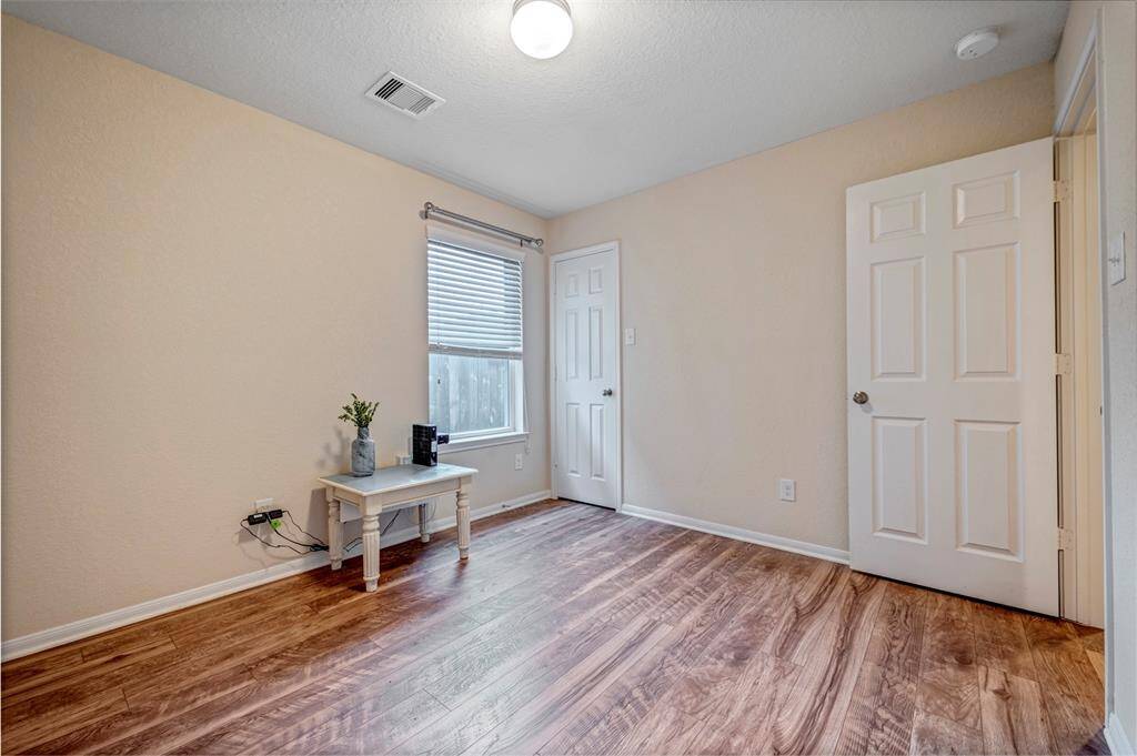 This bedroom features warm-toned wood like floors, neutral walls, and a bright window with blinds. It's cozy and inviting.