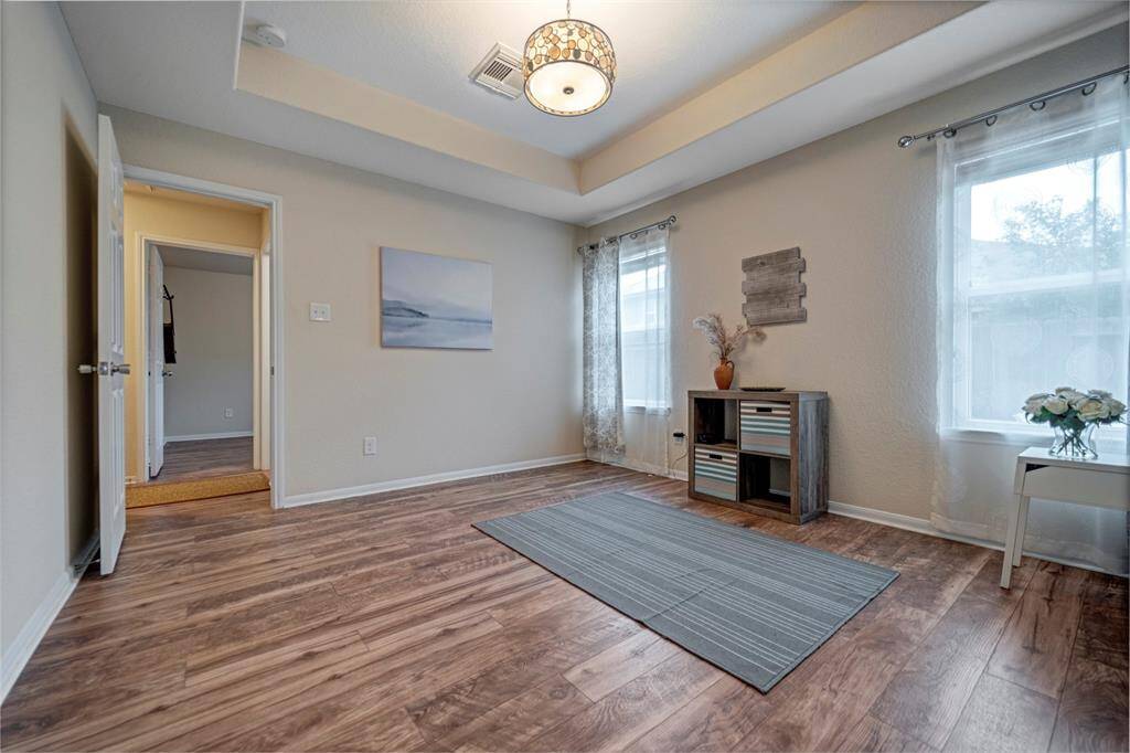 This spacious primary bedroom features a modern design with wood like flooring and a calming color scheme. Natural light from large windows, and an elegant ceiling light fixture. An en-suite bathroom is accessible, enhancing convenience and privacy.