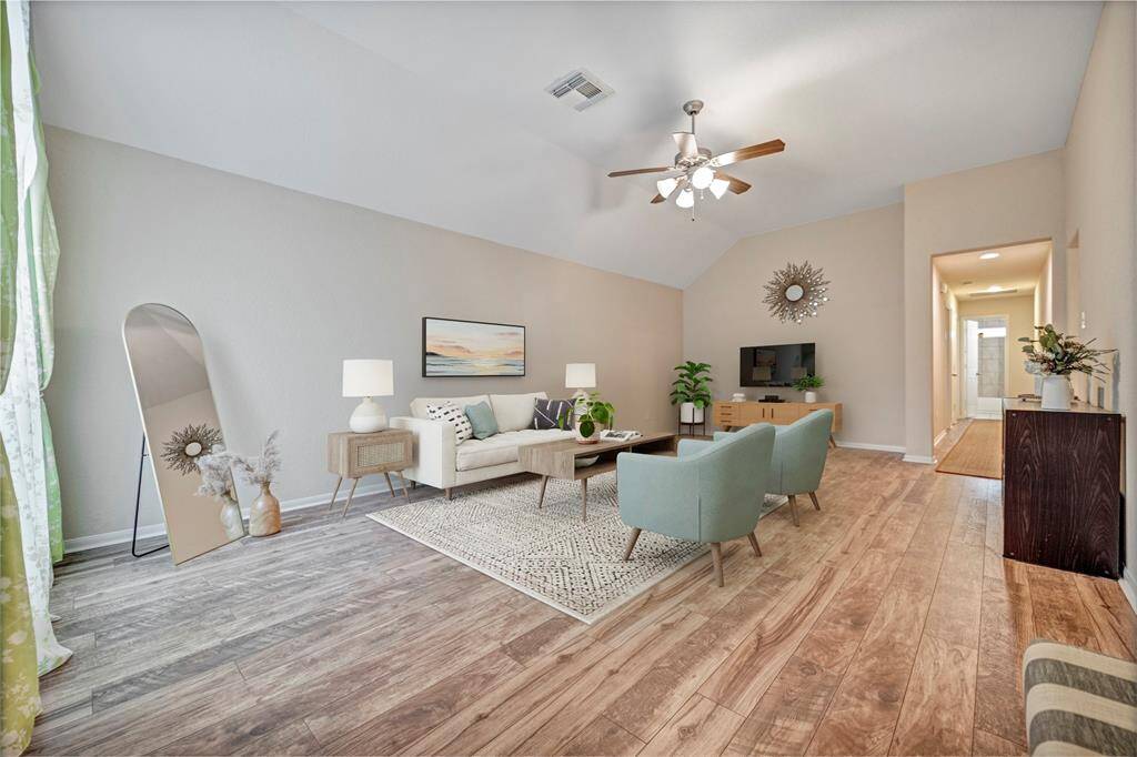 A spacious living room with vaulted ceilings, wood like flooring, and neutral walls.