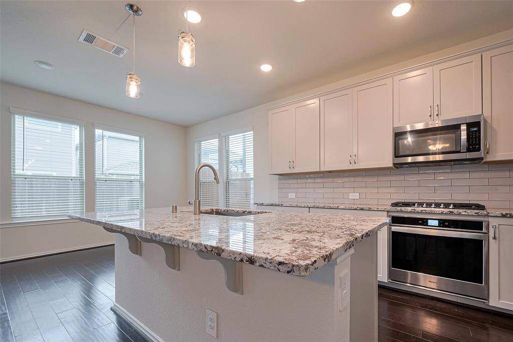 Under a soft glow from recessed lighting, the kitchen features generous cabinetry, sleek backsplash lines, and a central island with pendant lighting above—perfectly scaled for seating, prep, or gathering.