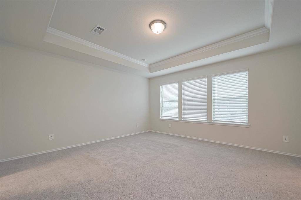 The primary bedroom offers a tranquil retreat, with soft carpeting, a tray ceiling for added dimension, and large windows that invite in plenty of daylight.