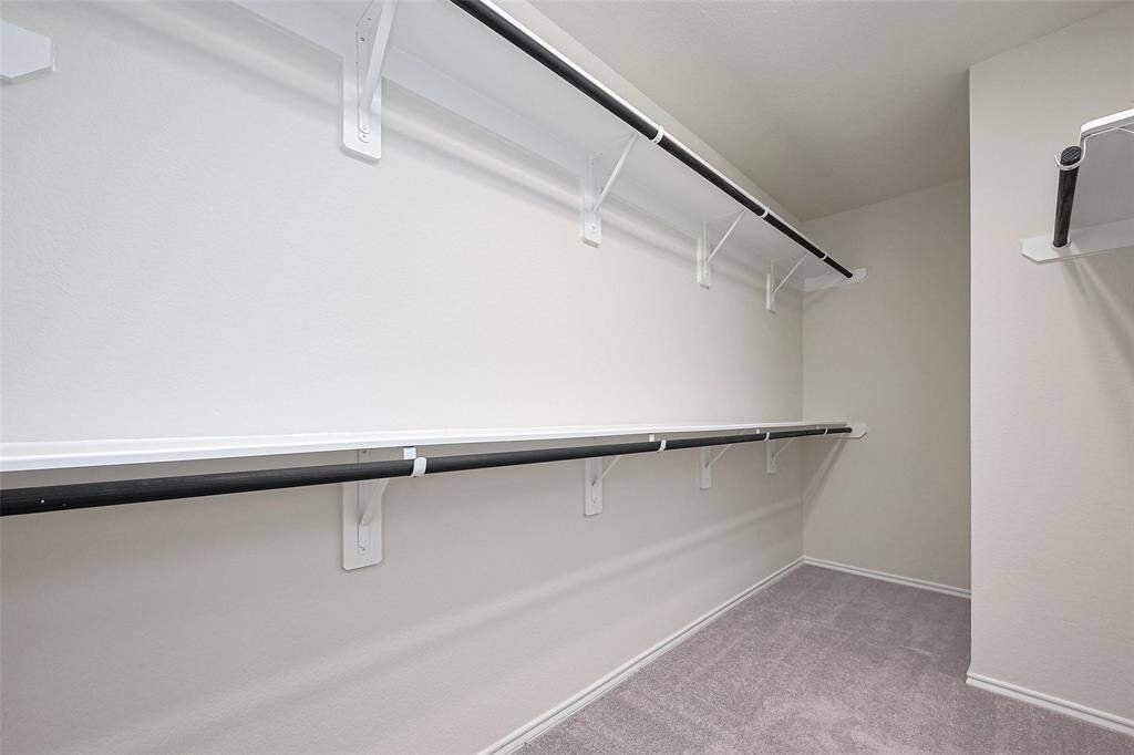 This full entry closet is both spacious and well-appointed, featuring built-in shelves and long hanging rods across multiple walls, all set over soft carpeting for comfort underfoot.
