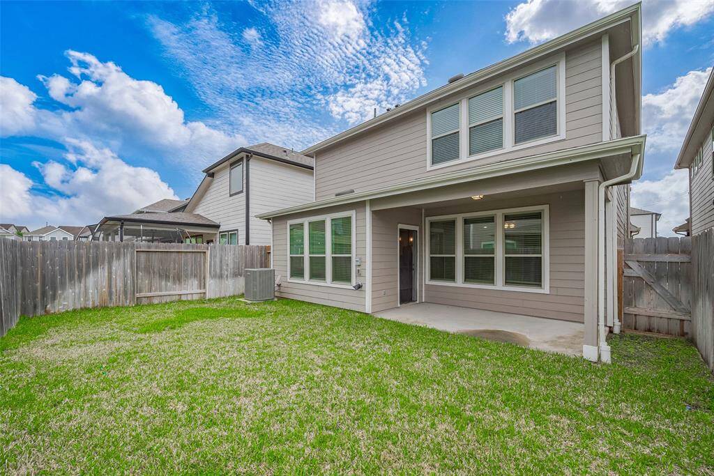 The rear of the home features a covered patio area overlooking the green yard—a perfect spot for outdoor lounging, shaded mornings, or evening get-togethers.
