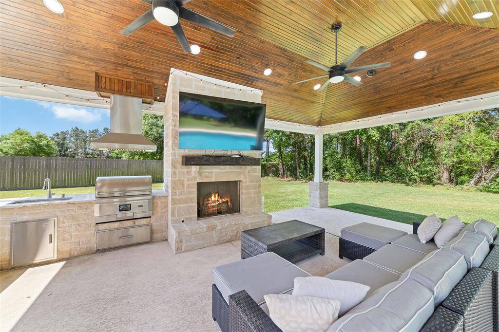 Covered cabana with TV, ceiling fan, and outdoor fireplace—an all-seasons lounge space for relaxed evenings or game day gatherings.