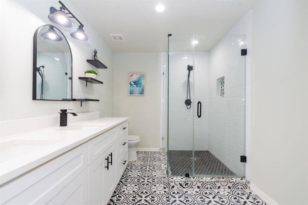 Stylish ensuite bathroom with a frameless glass shower, double sinks set in quartz countertops, and eye-catching black and white decorative tile flooring—combining function with modern design.