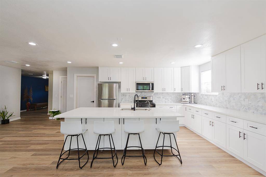 Modern and completely updated kitchen showcasing updated laminate flooring, sleek quartz countertops and island, abundant cabinetry for ample storage, and recessed lighting for a bright, clean look.