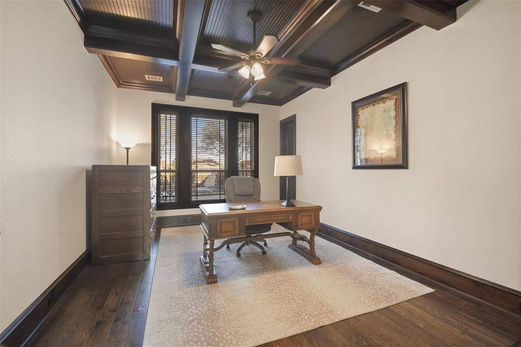 The home office is enclosed by French doors and has a beautiful coffered ceiling with crossed wood beams.