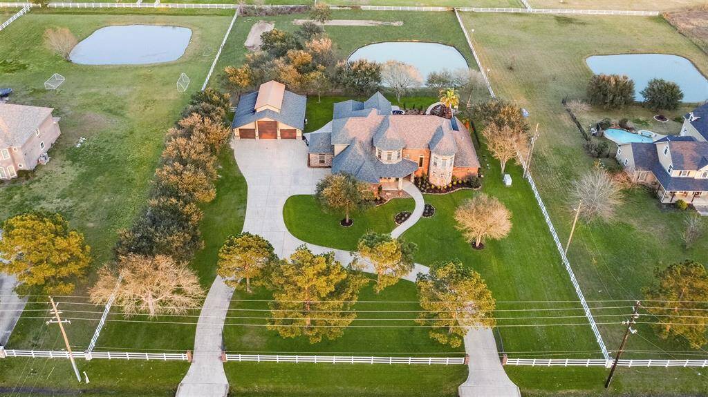 The property is fully fenced and features two gated entrances, a circle driveway, standalone garage/workshop, a stocked pond with a deck, and a backyard oasis with a pool that has a rock waterfall, cave & slide.