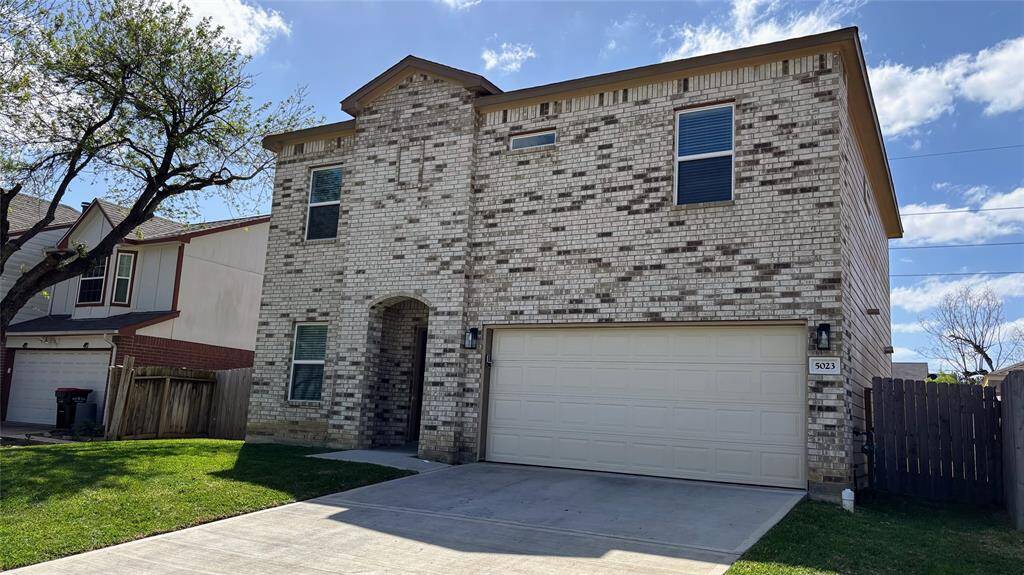 Front of the house with a spacious front yard. The property is fenced and has a mature tree providing shade.