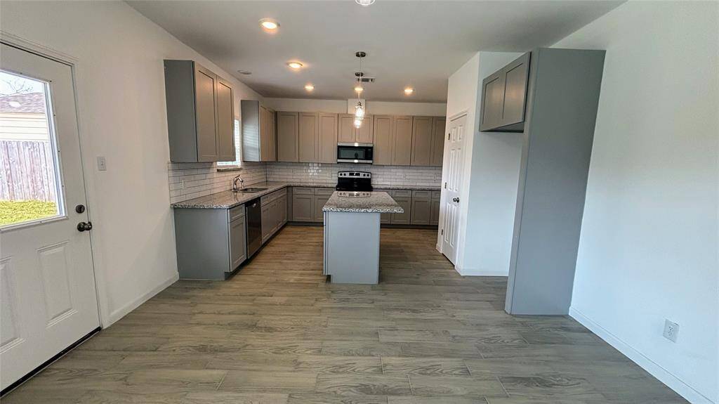 Bright, modern kitchen with gray cabinets, stainless steel appliances, and an island. Open layout with tile flooring and a view of the backyard through a large window.