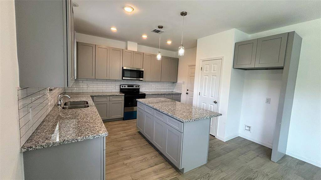 This modern kitchen features sleek gray cabinetry, granite countertops, and stainless steel appliances. It includes a spacious island, ample storage, and a stylish subway tile backsplash, creating a bright and functional space.