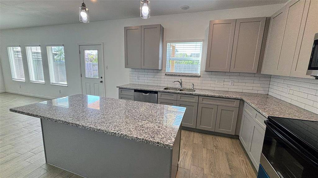 This kitchen features modern gray cabinetry, granite countertops, and a stylish tile backsplash.