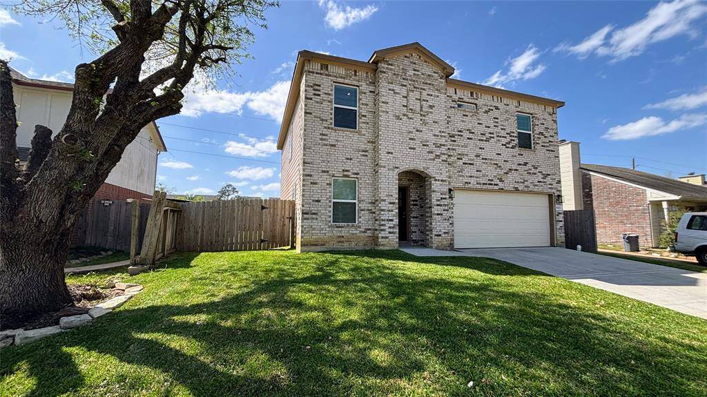 Front of the house with a spacious front yard. The property is fenced and has a mature tree providing shade.
