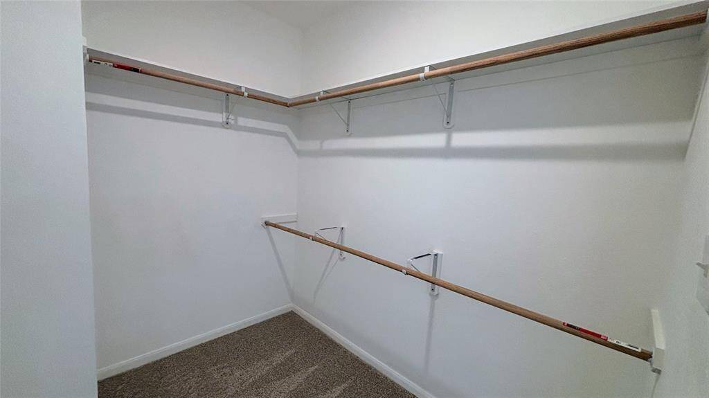 Spacious walk-in closet at Master with double hanging rods and carpeted flooring, offering ample storage space.