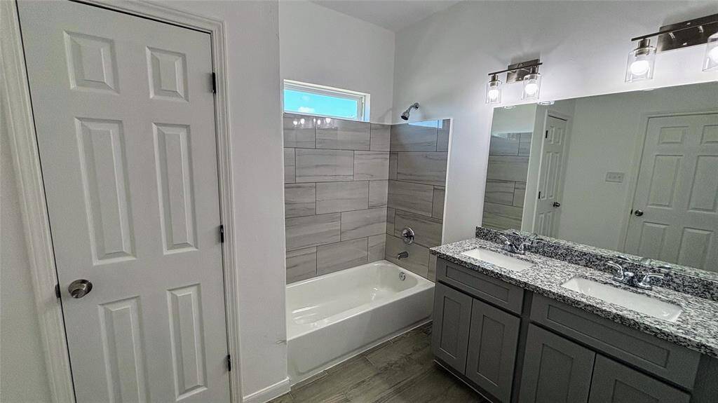 The master  bathroom features a modern design with a dual-sink granite countertop, a bathtub with sleek gray tile surround, and contemporary lighting fixtures.