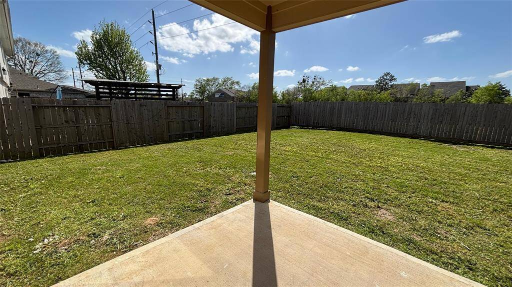 Spacious backyard with a well-maintained lawn, surrounded by a wooden fence for privacy, featuring a small covered patio area.
