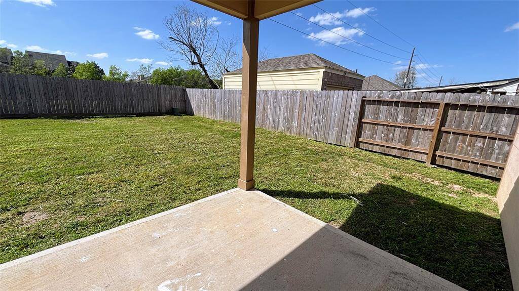 Spacious backyard with a well-maintained lawn, surrounded by a wooden fence for privacy, featuring a small covered patio area.