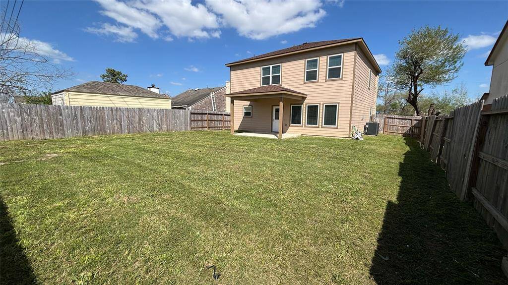 Spacious backyard with a well-maintained lawn, surrounded by a wooden fence for privacy, featuring a small covered patio area.