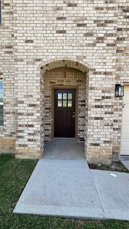 A welcoming entrance with a dark wooden door set in a light brick, featuring an arched doorway and adjacent garage. The entry path is concrete, bordered by a grassy area.
