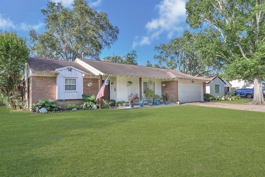 Charming single-story home with a brick facade, a well-maintained lawn, and mature trees. Features include a cozy front porch with seating, a spacious driveway leading to a double garage, and tasteful landscaping that adds to its curb appeal.