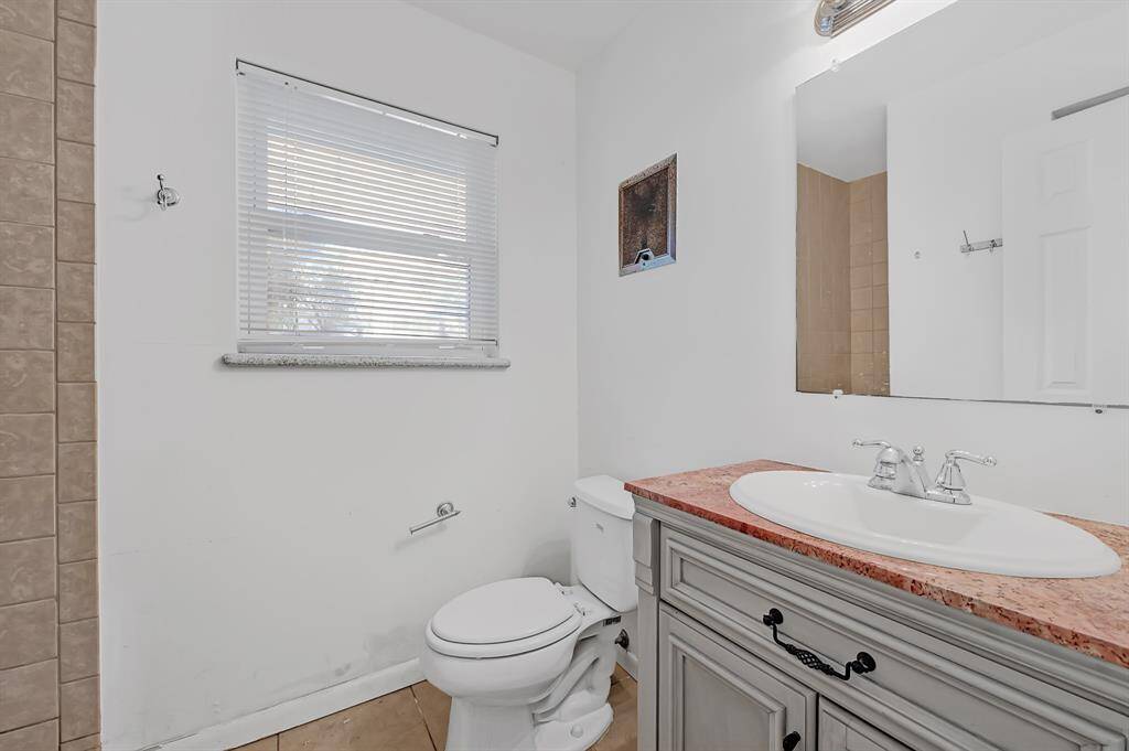 This bathroom features a simple design with a white vanity and sink, a large mirror, and a window with blinds providing natural light.