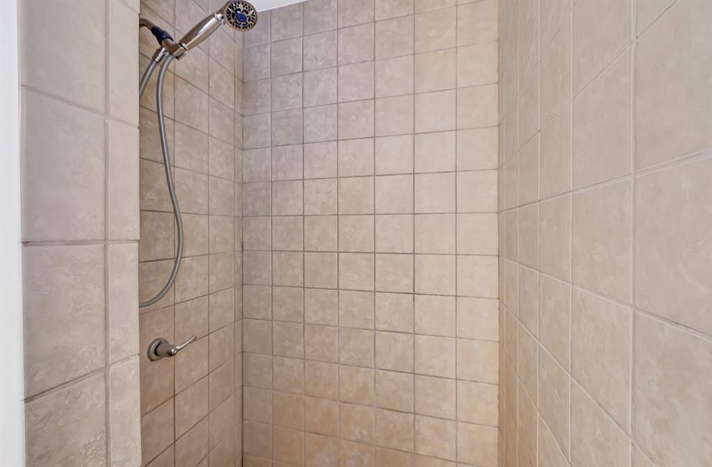 This photo shows a tiled shower area with neutral-colored tiles and a handheld showerhead, offering a clean and simple design.