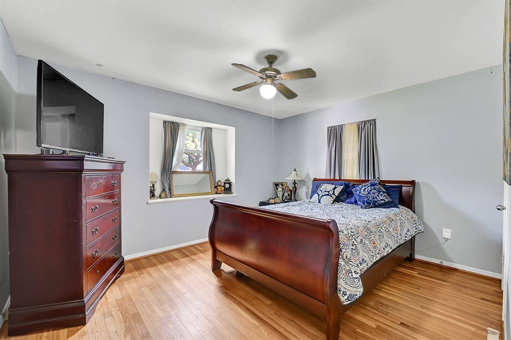This bedroom features a cozy setup with hardwood floors,  soft gray walls and two windows for natural light.