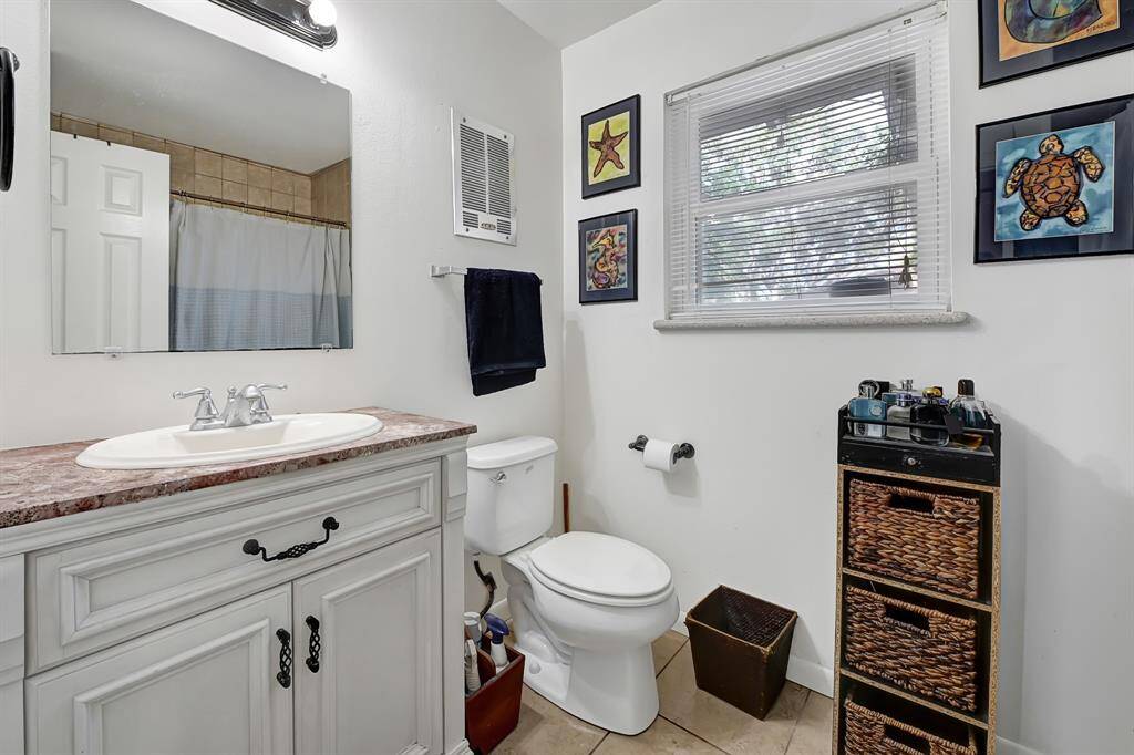 This bathroom features a classic vanity with a marble countertop and a large mirror. It has a shower-tub combo with a curtain, and a window for natural light.