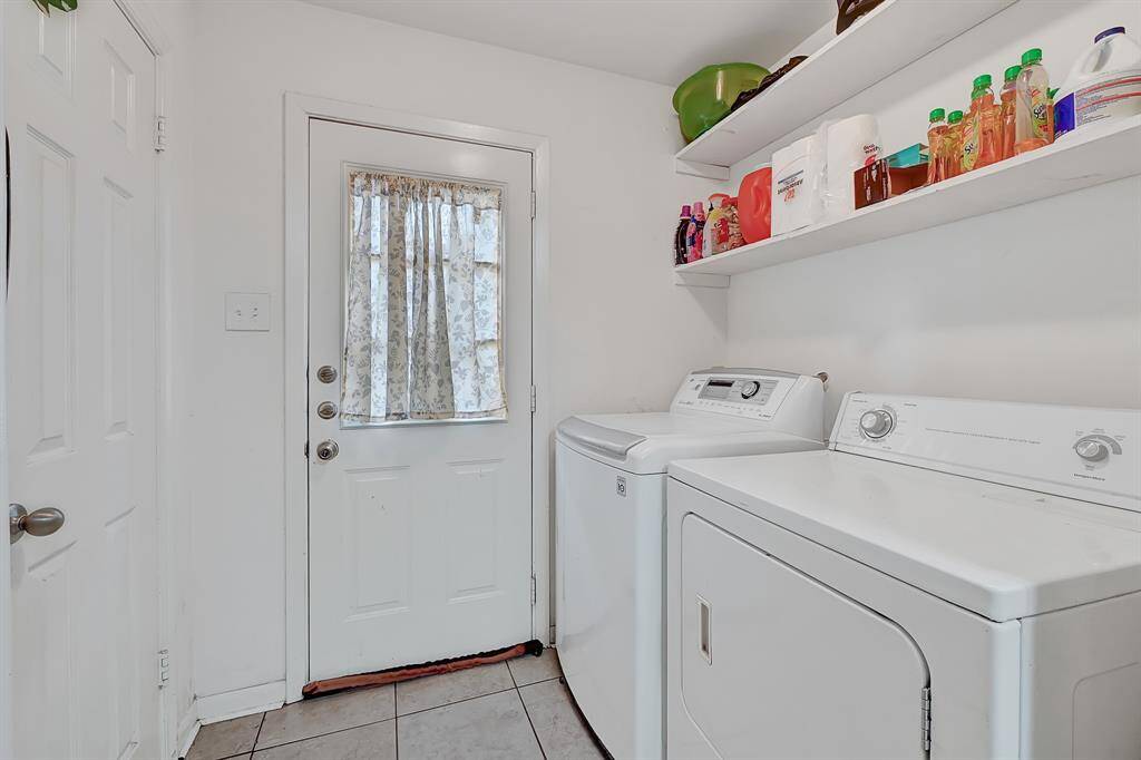 This laundry room features a washer and dryer, built-in shelving for storage, and a door providing natural light.