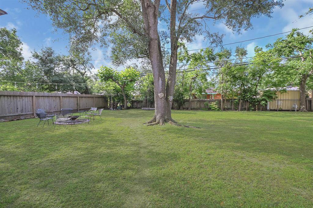 Spacious backyard with a large tree providing shade, a fire pit area with seating, and a wooden fence for privacy. Ideal for outdoor gatherings and relaxation.