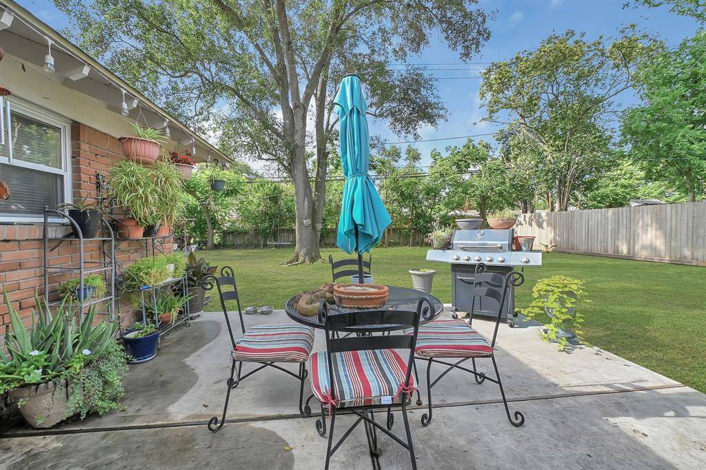 This inviting backyard features a cozy patio surrounded by lush greenery and the spacious lawn is shaded by mature trees, offering a serene and private retreat.