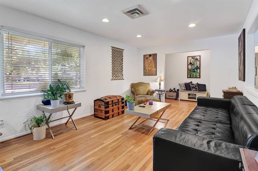 This inviting living room features hardwood floors, abundant natural light from a large window, and modern recessed lighting.