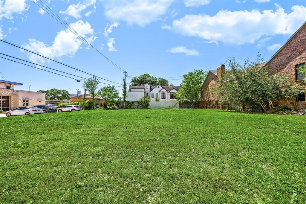 Spacious empty lot with lush green grass, surrounded by a mix of residential and commercial buildings. Ideal for new construction or investment.