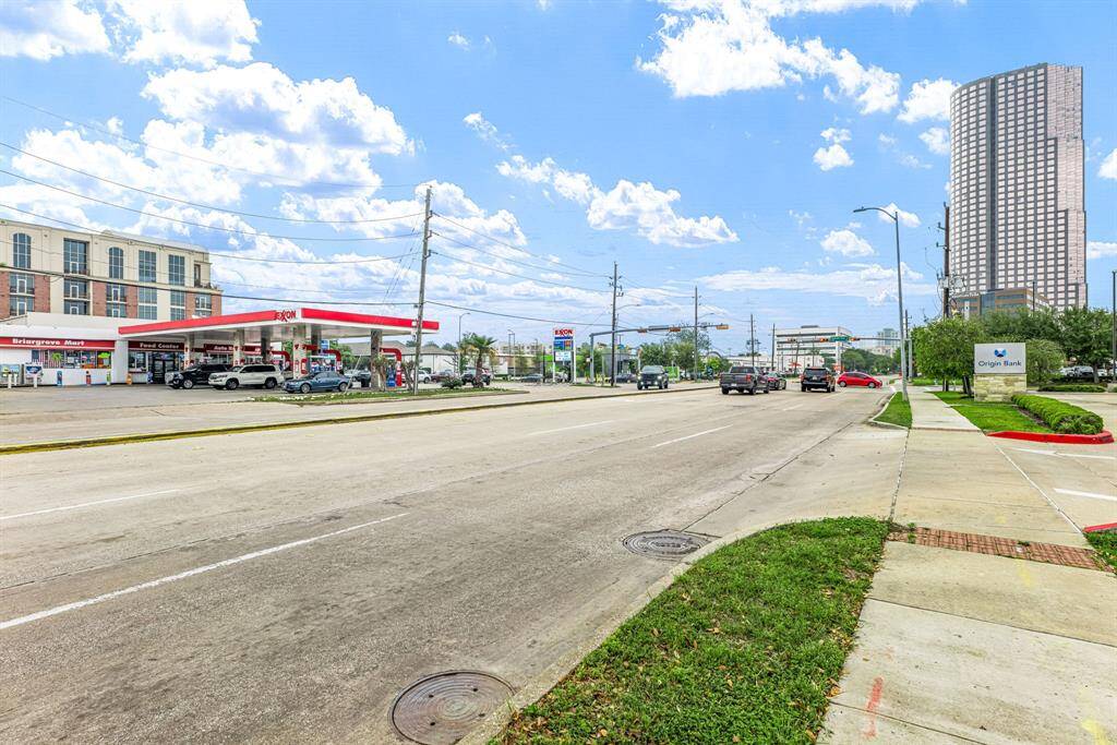 Urban street view with a gas station, bank, and tall building nearby. Sidewalks and a well-maintained road are present, offering convenience and accessibility.