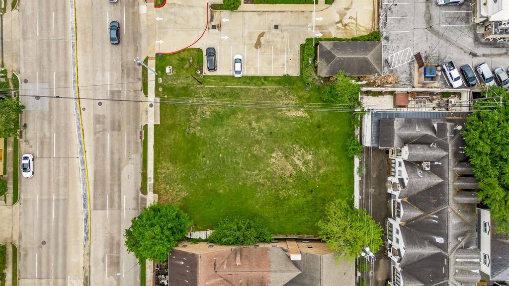 This aerial photo showcases a vacant plot of green land surrounded by residential and commercial buildings, with a nearby road providing easy access. Ideal for new construction or investment.
