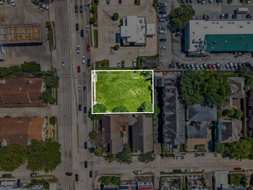 This aerial photo shows a vacant grassy lot in a residential area. It's surrounded by roads and nearby buildings, offering a blank canvas for development in a well-established neighborhood.