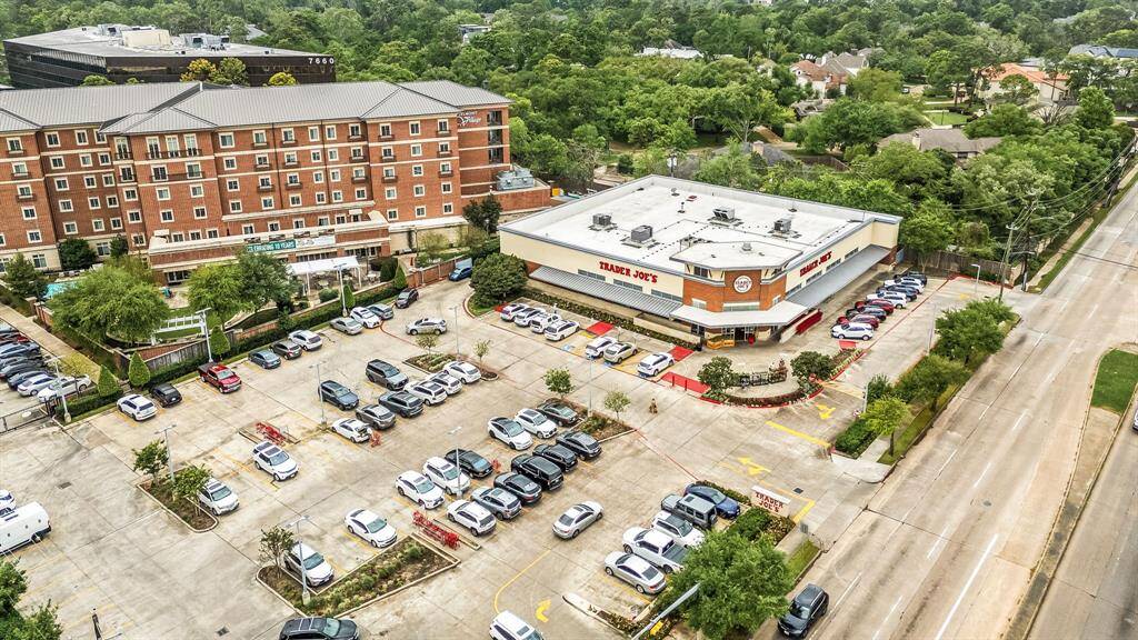 The photo shows a vibrant area with a Trader Joe's and a large apartment building nearby. The location includes ample parking and is surrounded by green spaces and residential neighborhoods, suggesting a convenient and desirable setting for potential home buyers.
