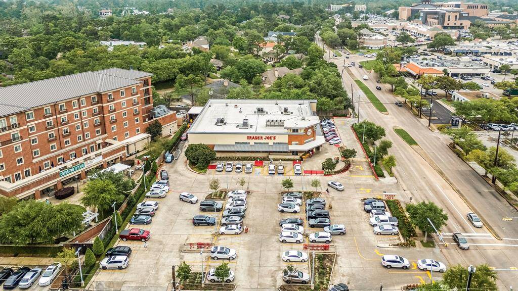 Aerial view of a busy commercial area featuring a grocery store with ample parking. It's surrounded by greenery and nearby residential buildings, offering convenient access to shopping and services.