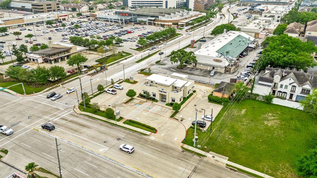 This aerial photo shows a commercial area with a bank and various retail stores, including a large grocery store, along a busy street. Nearby are residential homes and ample parking, highlighting a convenient location with easy access to amenities.