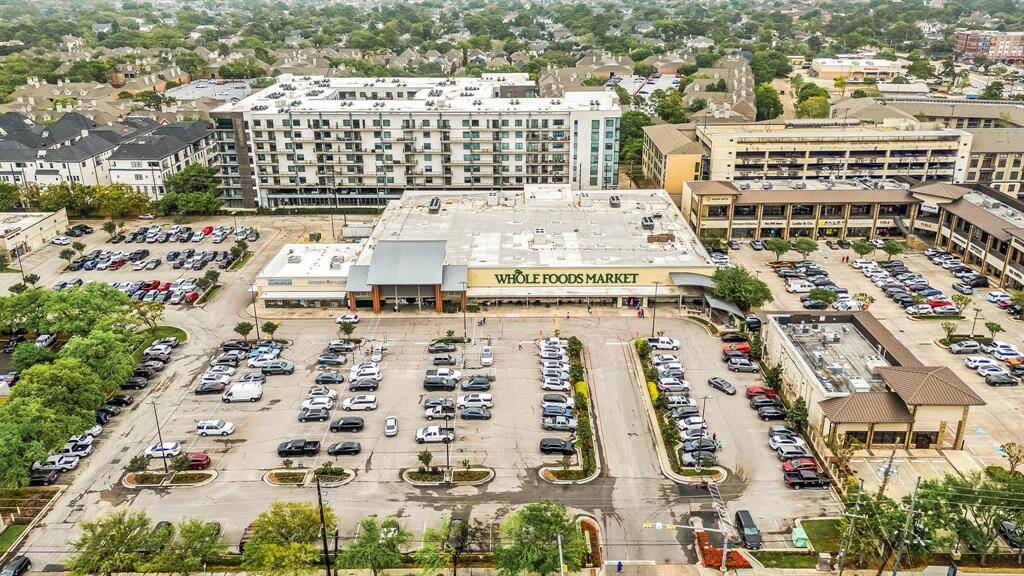 This aerial photo shows a bustling urban area with a Whole Foods Market at the center, ample parking, and nearby residential and commercial buildings, indicating a convenient and vibrant neighborhood.