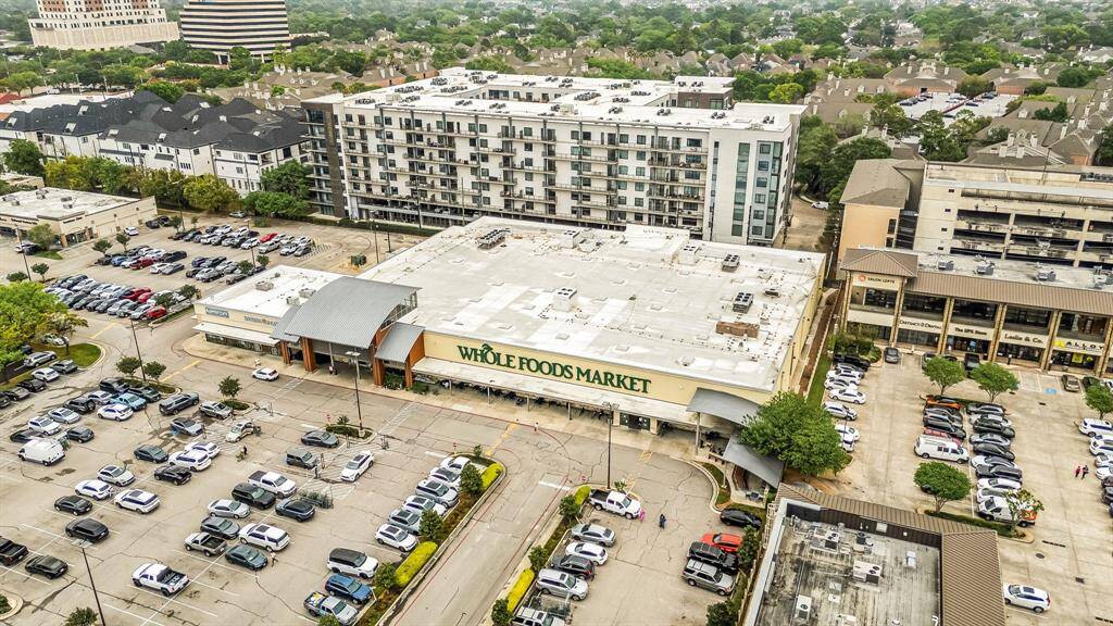 This aerial photo features a bustling urban area with a Whole Foods Market at its center. Surrounding it are residential buildings, ample parking spaces, and nearby commercial establishments, offering a convenient lifestyle with shopping and amenities close by.