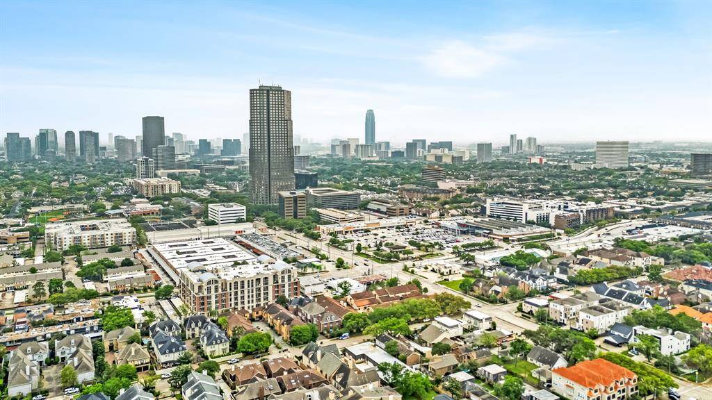 This aerial photo showcases a vibrant urban area with a mix of residential neighborhoods and commercial buildings. The skyline features several tall buildings, indicating a bustling city environment. The surrounding area includes green spaces and well-organized streets, suggesting a blend of modern living and convenience.