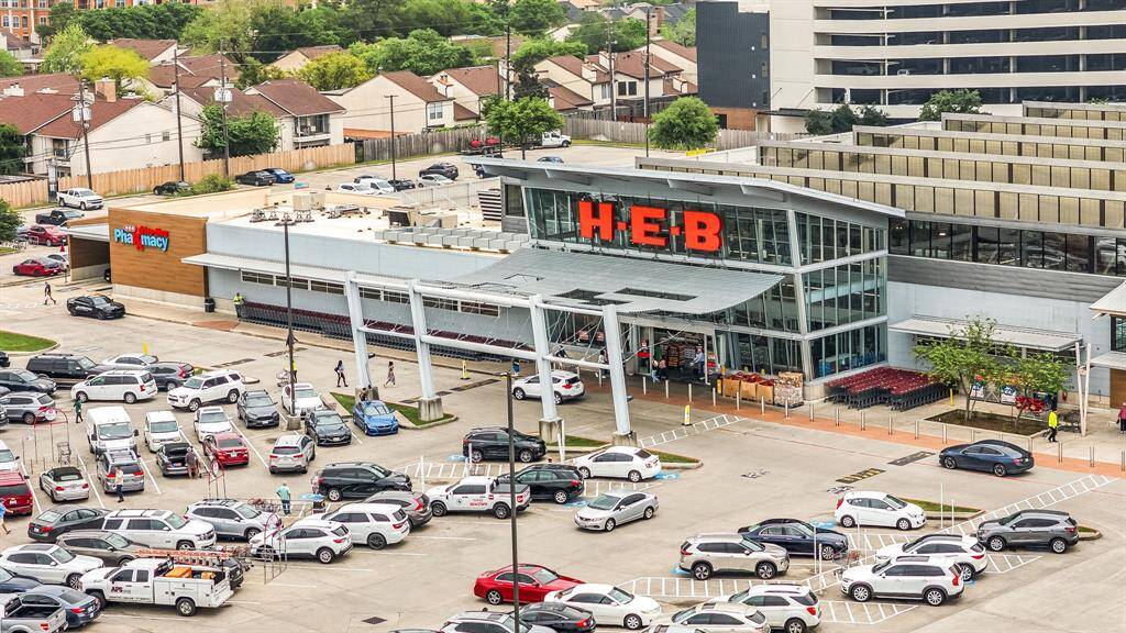 This photo shows a large H-E-B grocery store with a pharmacy, ample parking, and residential homes nearby, highlighting convenient access to shopping and amenities.