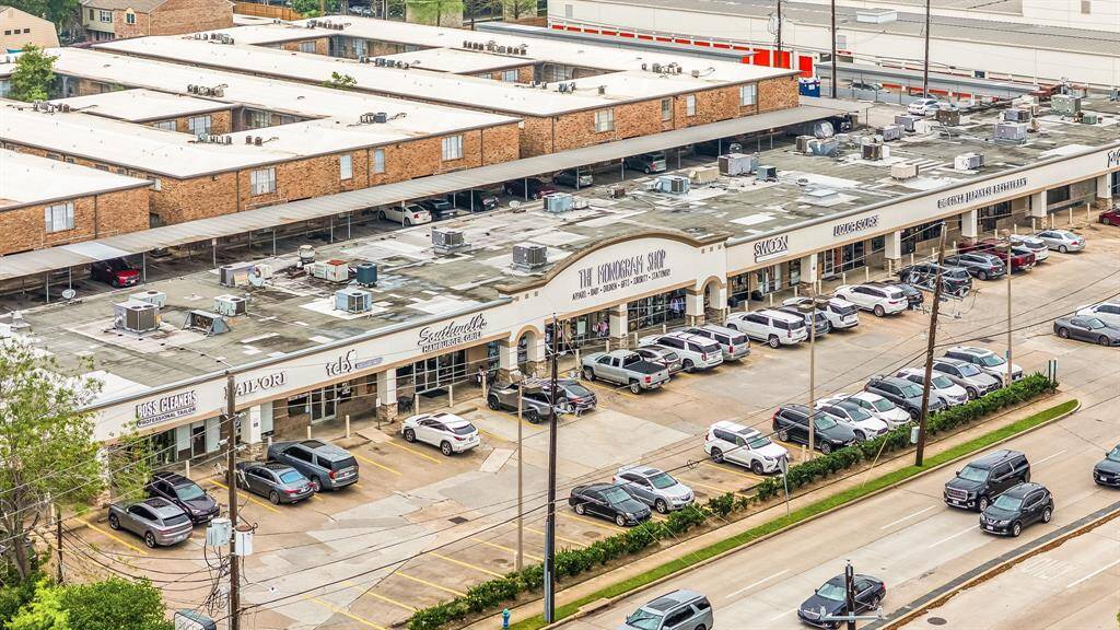 This photo shows a shopping center with various businesses, ample parking, and easy street access. The architecture features a flat roof and brick exterior, providing a practical and convenient location for shopping and services.