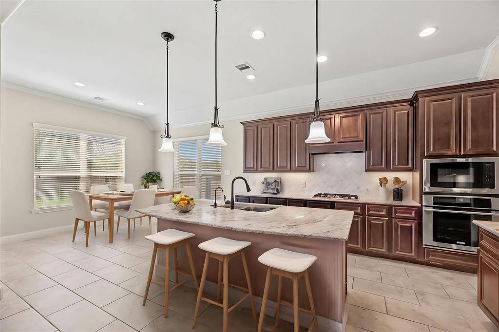 Your chef-inspired kitchen is ready to impress! This beautifully designed space offers gleaming granite countertops, a coordinating stone backsplash, and sleek stainless steel appliances. The rich cabinetry is perfectly complemented by under-cabinet lighting and recessed lighting, creating a bright and inviting ambiance. At the heart of it all, a sprawling island with breakfast bar seating. - virtually staged
