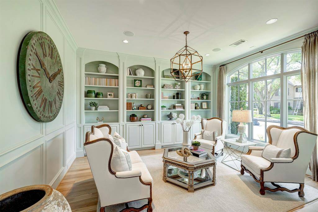 Elegant formal living room featuring street views, wainscoting, modern light fixture, custom built-ins, and rich hardwood floors.