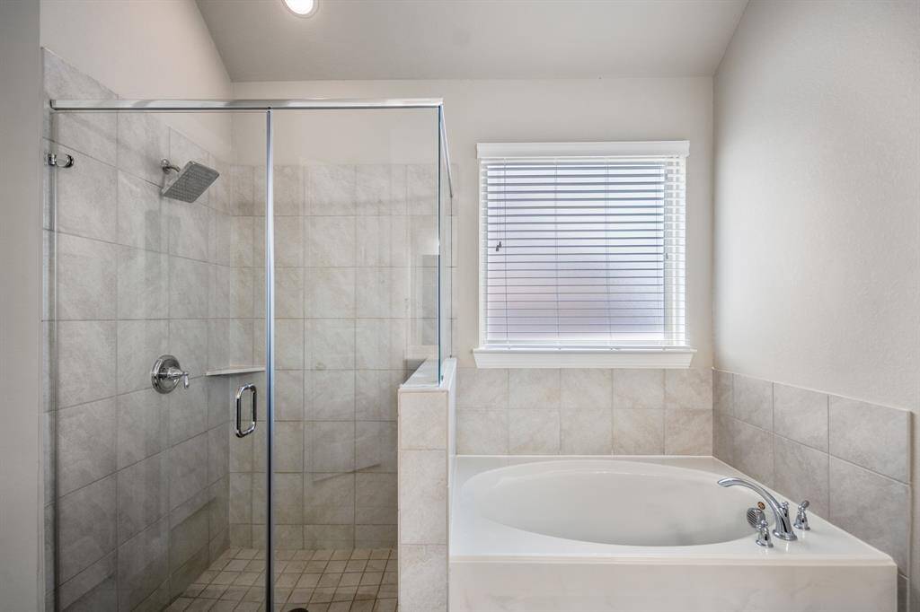This primary bathroom includes a spacious shower with mudset flooring, glass surround, and neutral tile. It's completed with a large garden tub allowing for a tranquil retreat.