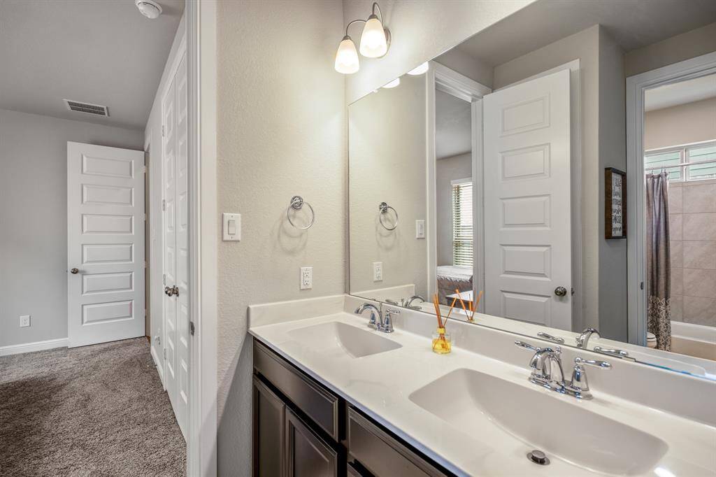 Located between two of the secondary bedrooms, this full bathroom offers additional privacy with a separated vanity area from the tub and shower making it easy to share and get ready. It features dual sinks, wood cabinets, white countertops, and linen closet.