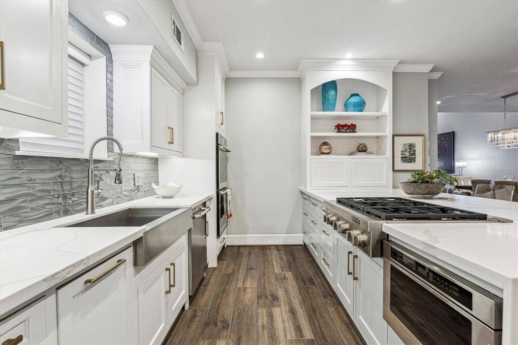 The Jennair 6-burner gas range top and a conveniently placed built-in microwave are designed to accommodate both everyday meals and gourmet cooking. The spacious island with quartz countertops and seating adds to the space's functionality and style, while soft-close cabinetry enhances the kitchen's modern convenience.